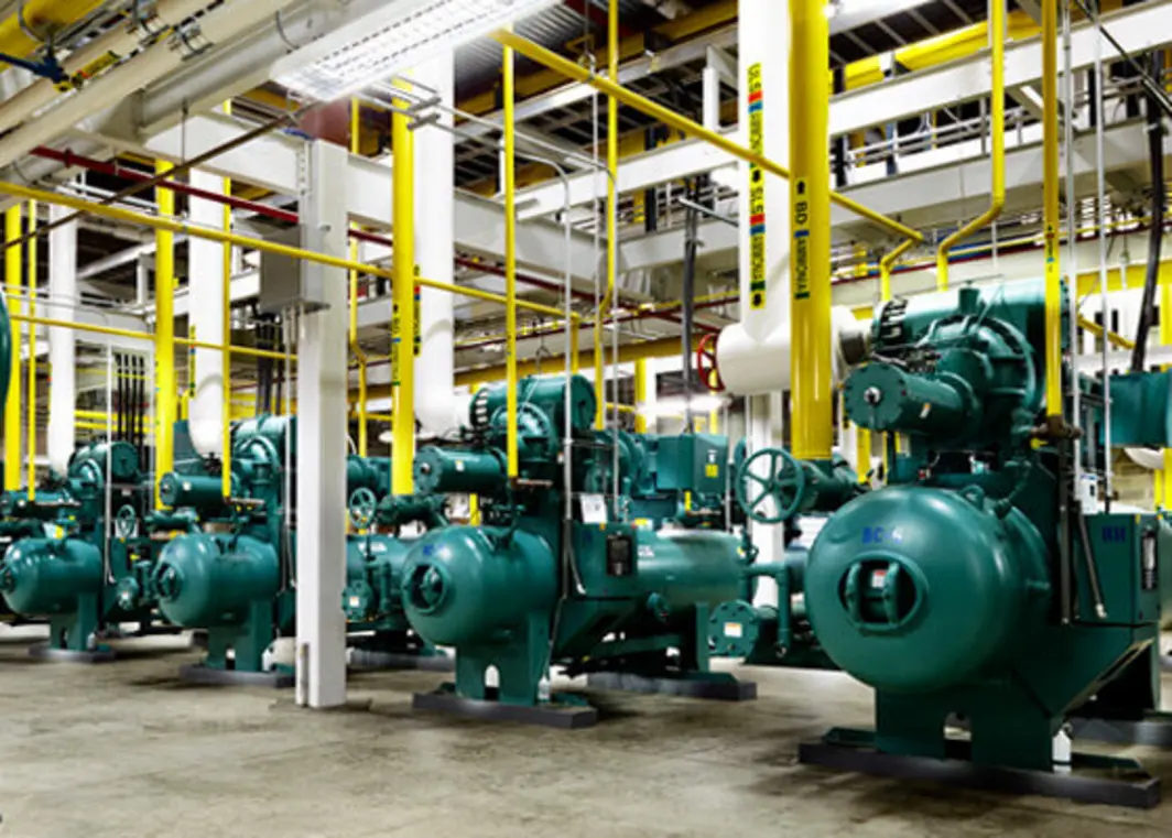 Industrial refrigeration equipment with multiple large green compressors and yellow pipes in a facility.