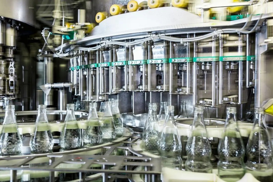 Industrial beverage bottling machine filling glass bottles on a production line.