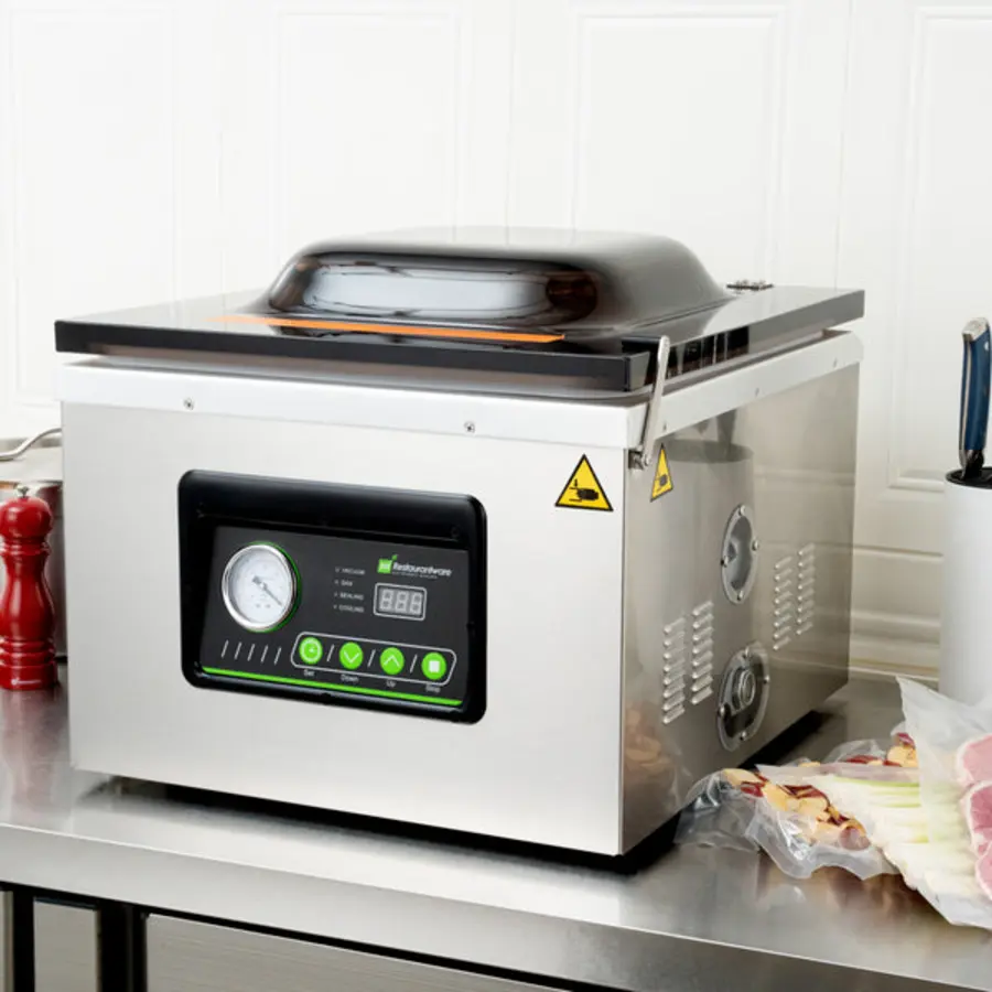 Stainless steel chamber vacuum packaging machine with a domed lid, control panel, and food packages beside it.