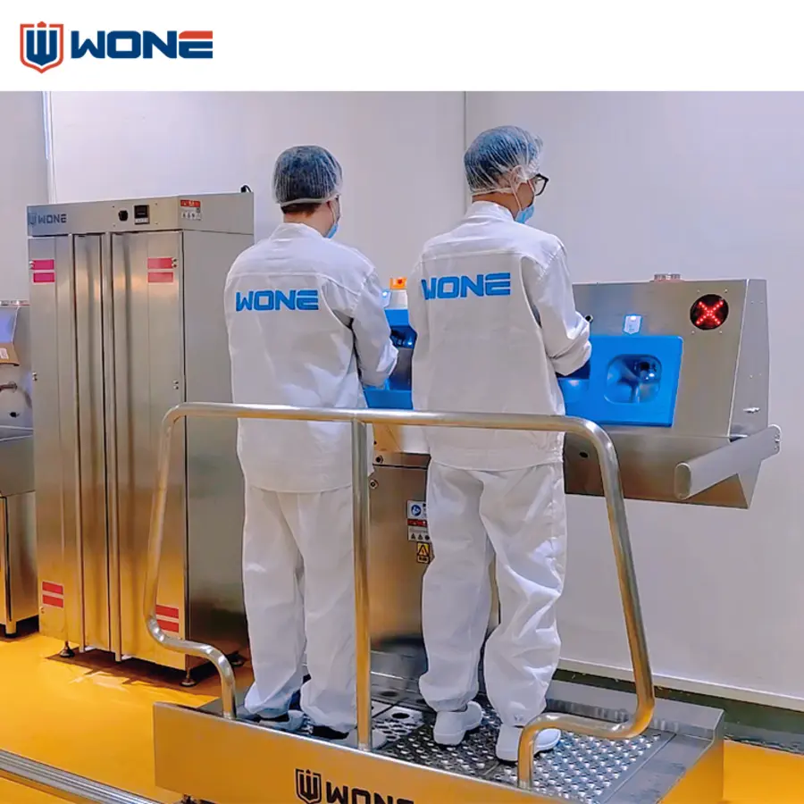 Workers in white protective clothing operate stainless steel equipment at a controlled entry point with hygiene barriers.