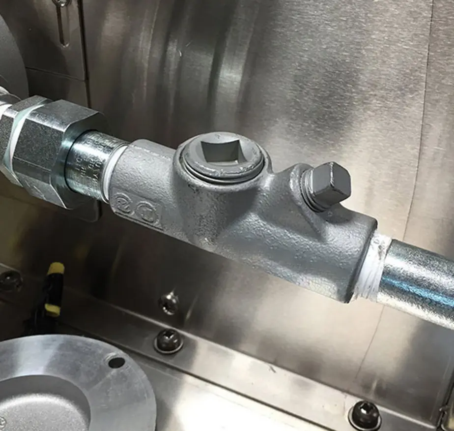 Gray conduit sealing fitting with plugs connects rigid metal conduits inside a stainless-steel enclosure.
