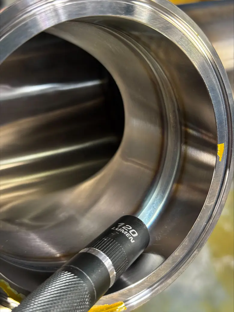 A close-up of a welded stainless steel pipe used in food processing equipment, showing smooth, polished surfaces and precise welds.