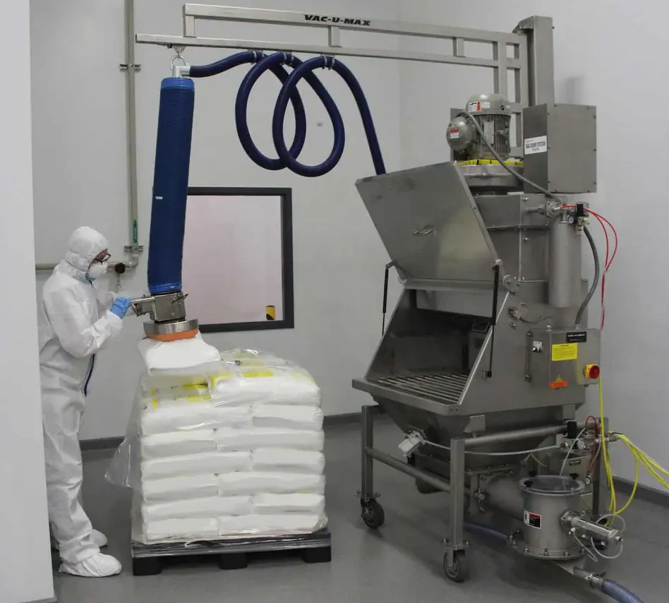 Worker in protective gear using a vacuum dust collection system with powdered material.