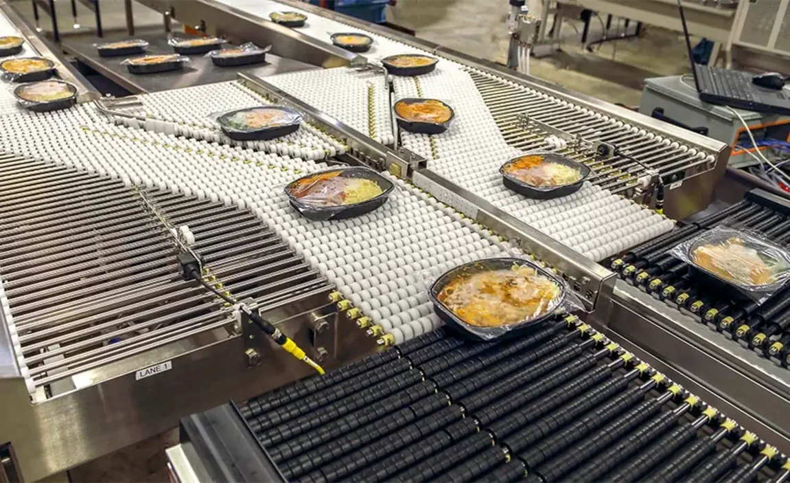 Packaged meals move along multiple conveyor belts in an industrial food production facility.