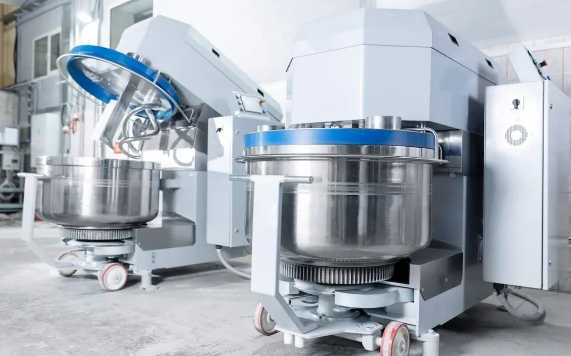 Industrial food-processing machinery featuring large mixers with stainless steel bowls and gear systems.