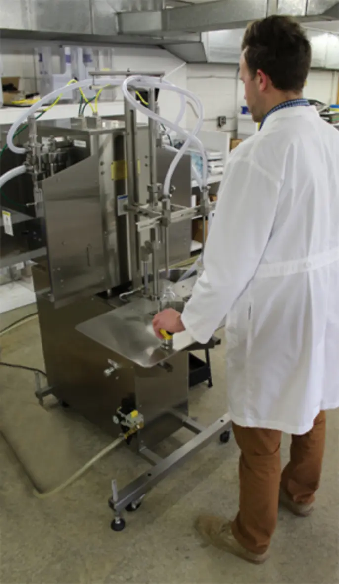 A worker in a lab coat operates a meat processing machine in a workshop setting.