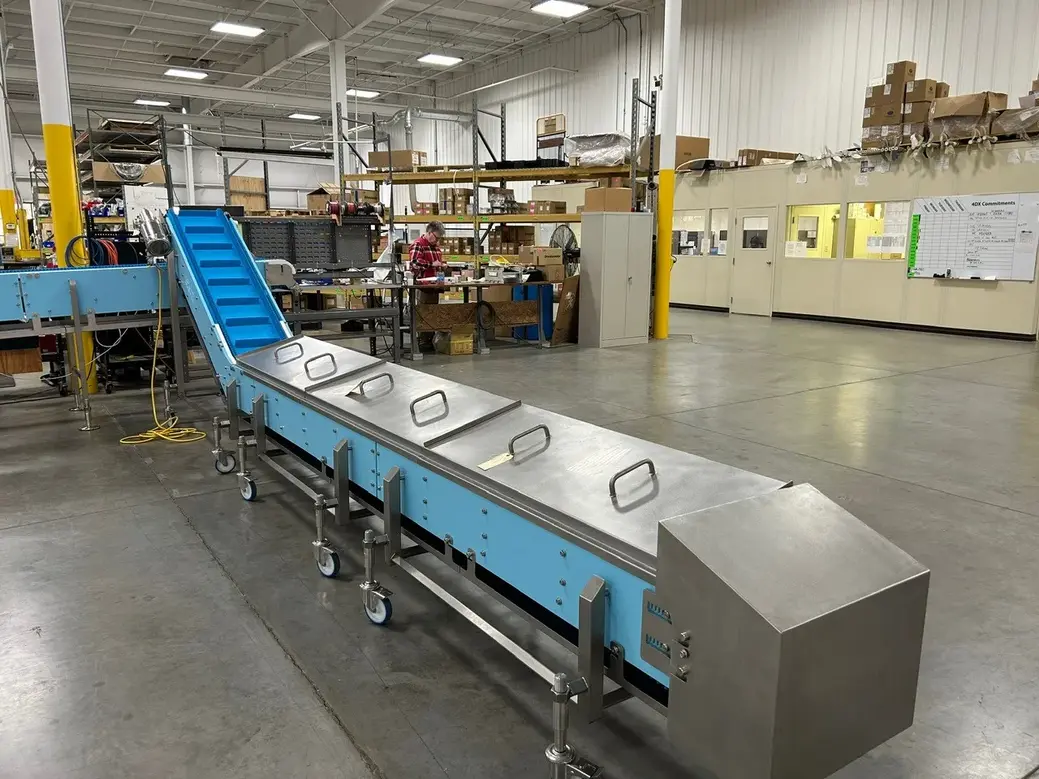 Conveyor system with a blue incline and stainless steel surface in a manufacturing facility.