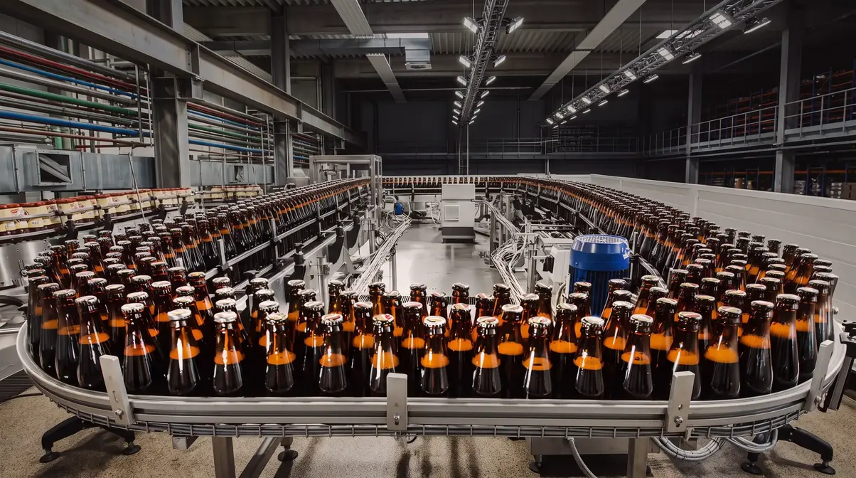 Bottles on a conveyor belt in an industrial brewery setting.
