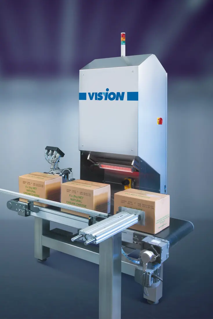 In-line vision inspection machine examining cardboard boxes on a conveyor with overhead camera and signal tower.