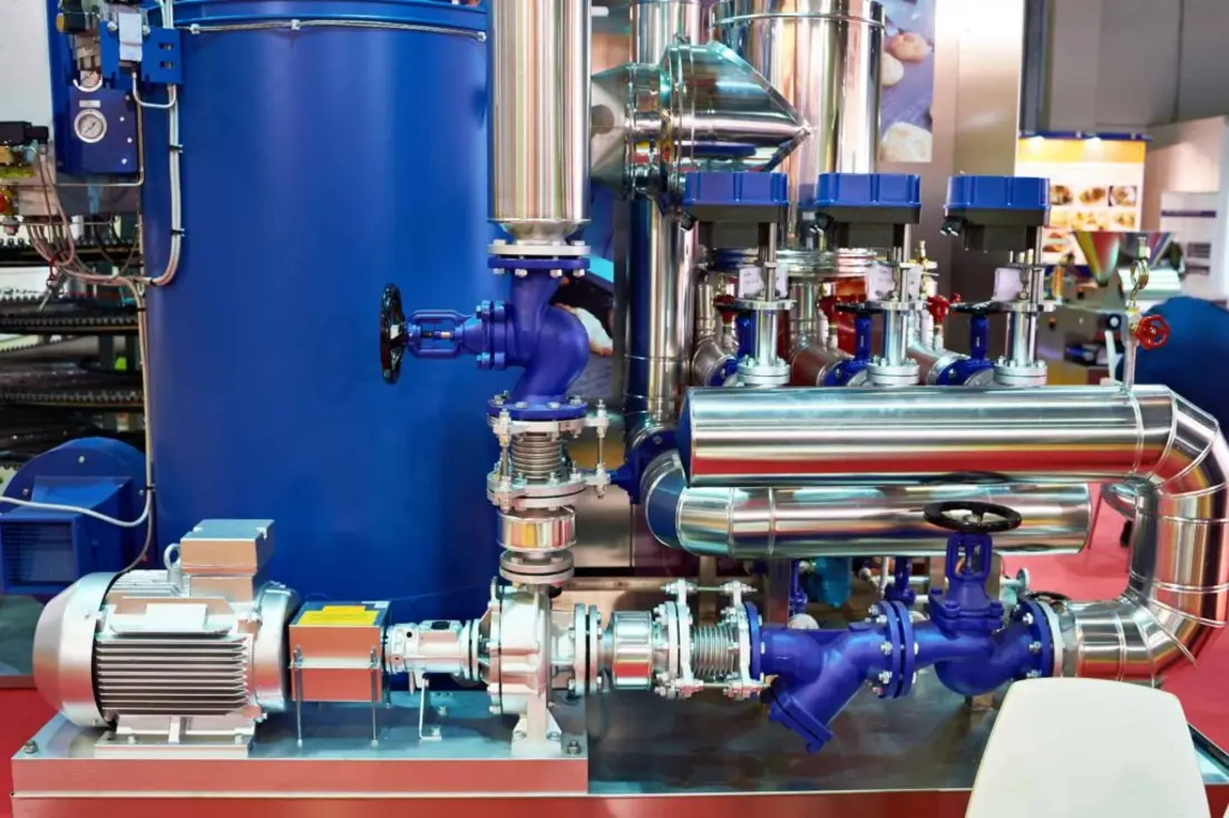 Stainless steel pilot processing equipment with blue vessels, pumps, valves, piping, and an electric motor.