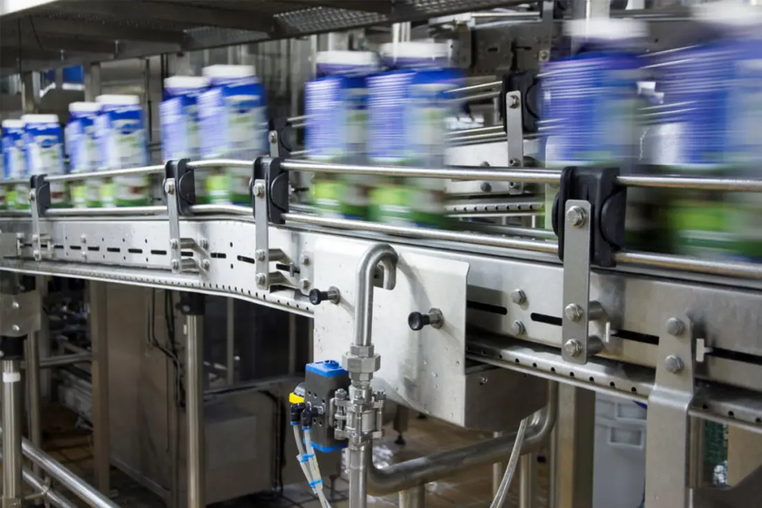 Food-processing conveyor carrying blurred blue-and-white containers through stainless steel machinery.