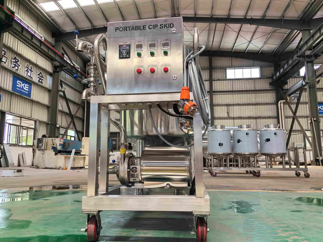 Stainless steel portable CIP skid with control panel, hoses, pump, and wheeled frame in an industrial facility.