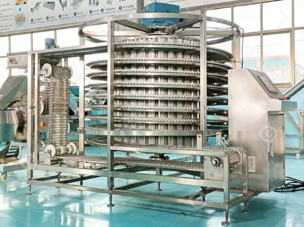 Industrial spiral freezer with multiple stacking trays in a food-processing environment.